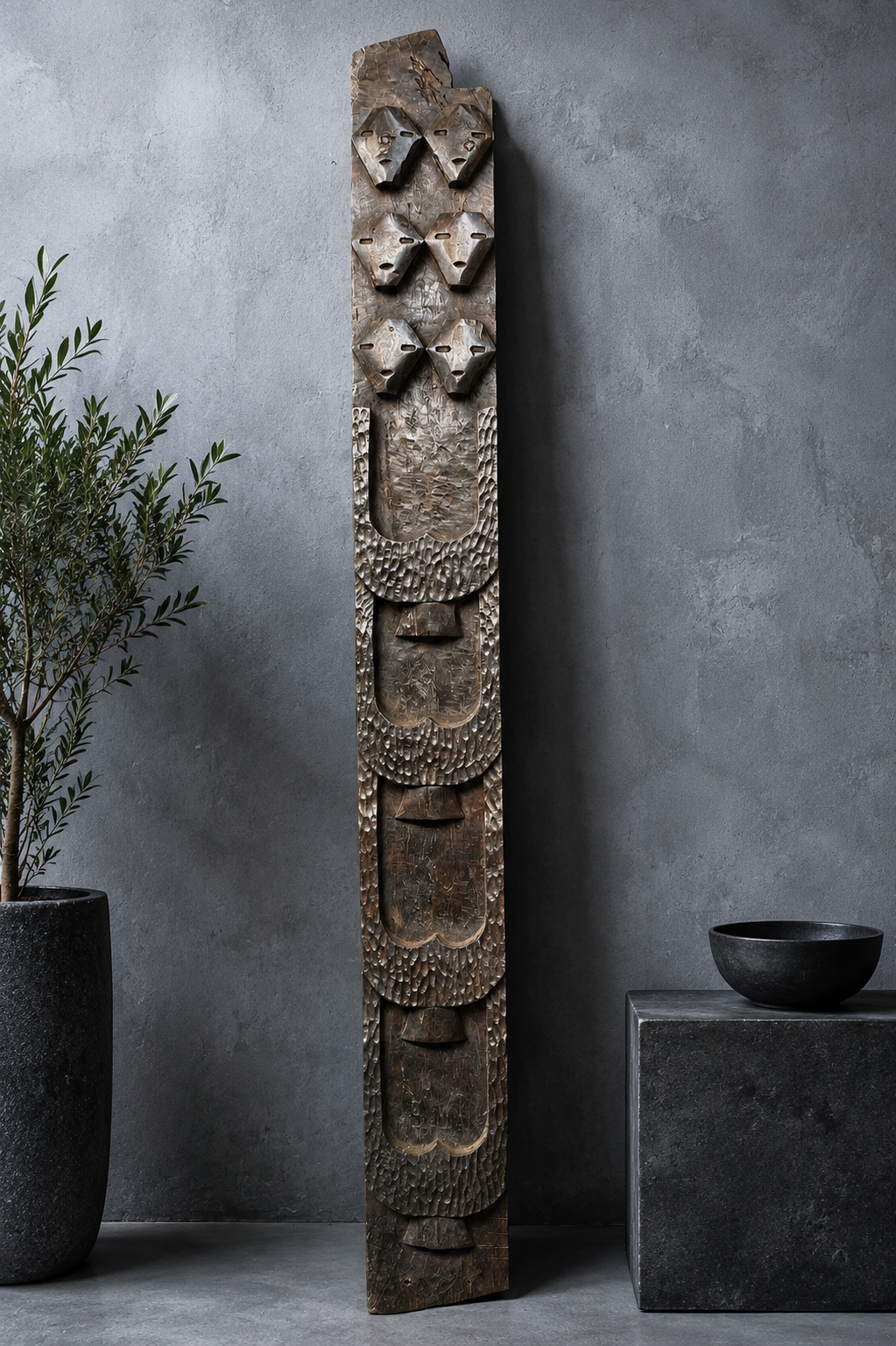 Antique Naga tribal totem panel with six carved mask faces against a grey concrete wall